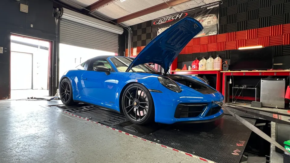 A blue Porsche 911 Targa GTS on a dyno at Jotech Motorsports, with its hood open, ready for performance tuning.