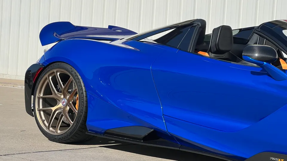 A blue McLaren 765LT convertible with gold HRE wheels, carbon fiber side mirrors, and a large rear wing.