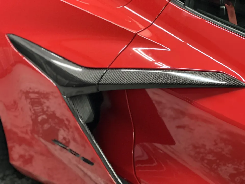 Close-up of the carbon fiber side vent and trim on a red C8 Corvette, highlighting exterior aero details.