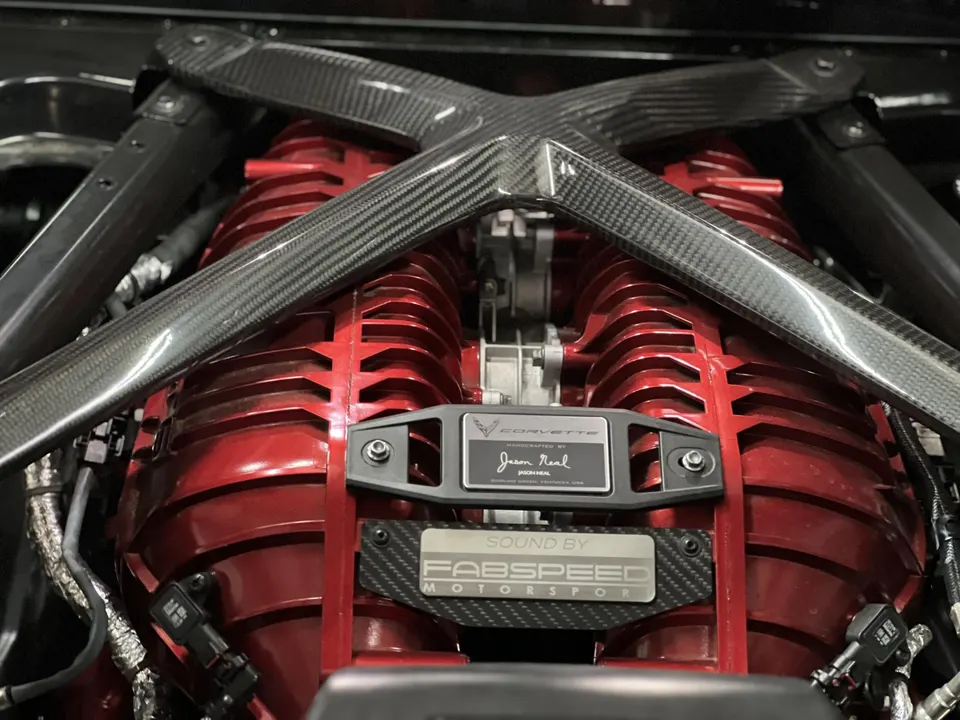 Close-up of a C8 Corvette engine bay featuring a red intake manifold and carbon fiber bracing, with Fabspeed Motorsport badging.