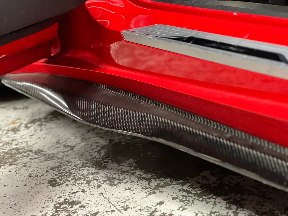 Close-up of a red car's carbon fiber side skirt and rocker panel.