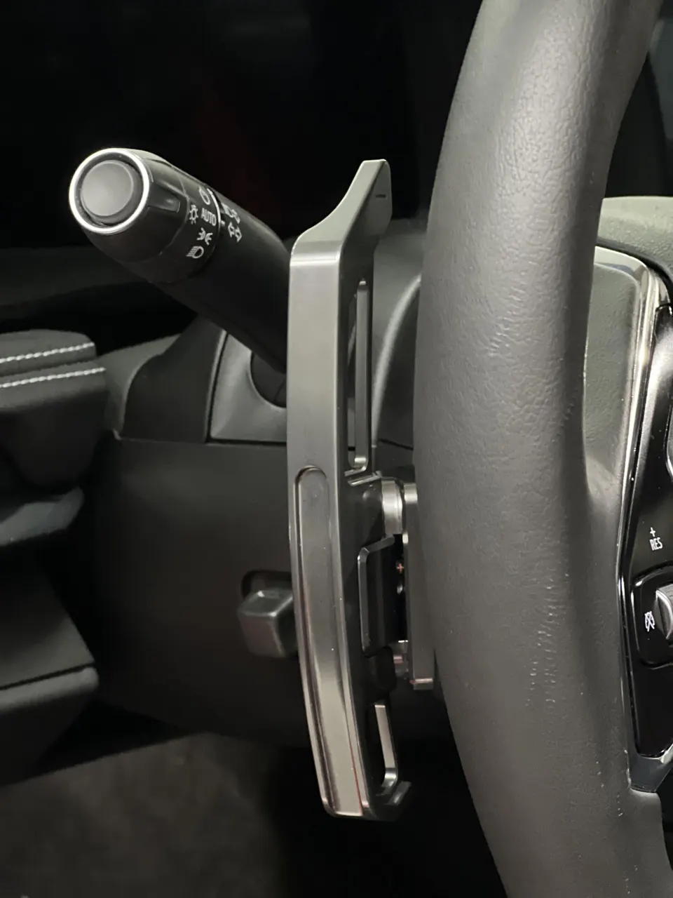 A close-up of a car's steering wheel and extended paddle shifter, showing the interior detail.