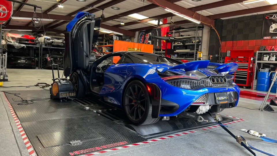 A blue McLaren 720S with its butterfly doors open, strapped to a dynamometer for performance testing at Jotech Motorsports.