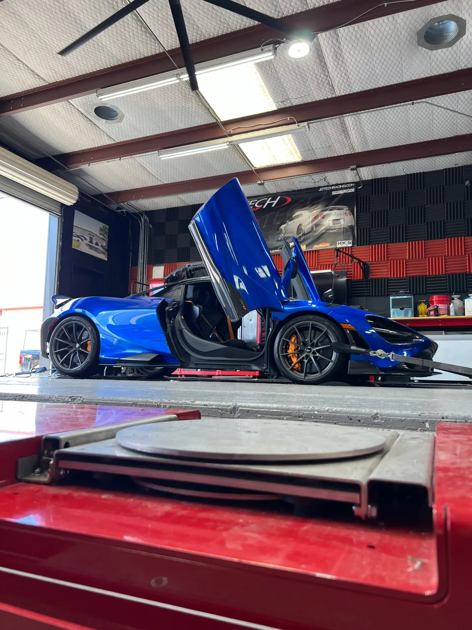 A blue McLaren supercar strapped to a dyno in a performance tuning shop, ready for a power run.