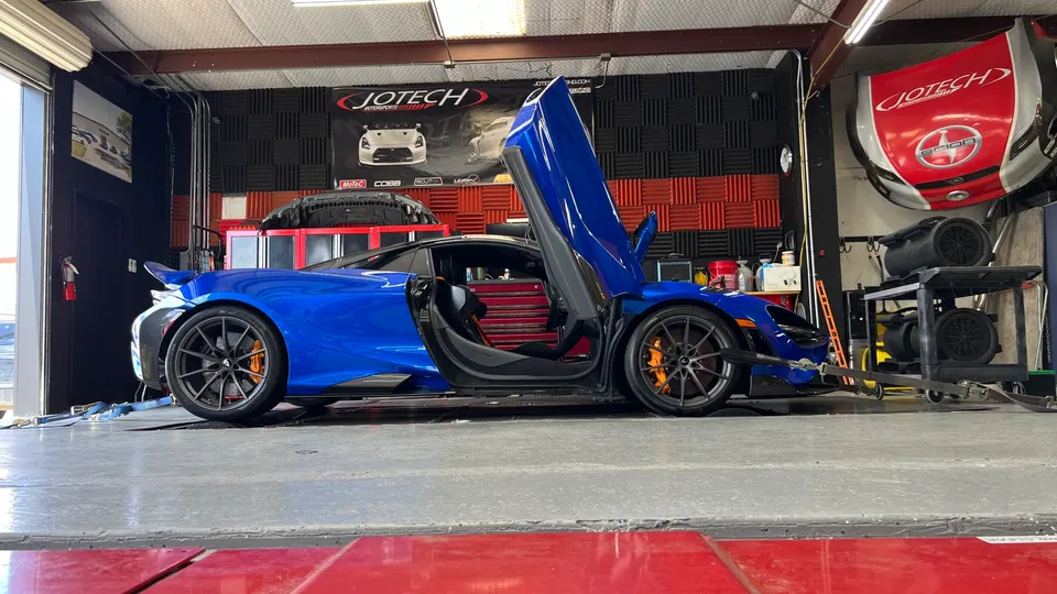 A blue McLaren 720S with its doors open, strapped to a dynamometer at Jotech Motorsports for performance testing.