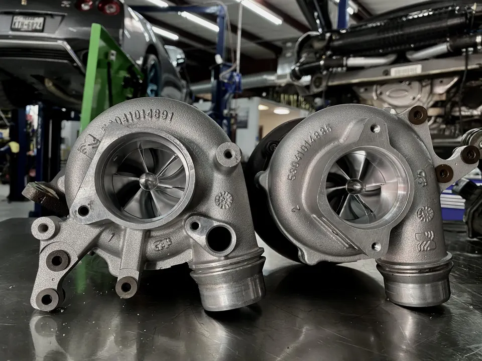 Two new turbochargers on a workbench in a performance tuning shop, with a Nissan GT-R on a lift in the background.