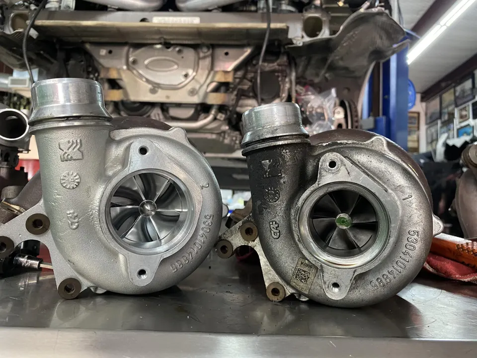 New and old turbochargers on a workbench in a performance shop, with a car on a lift in the background.
