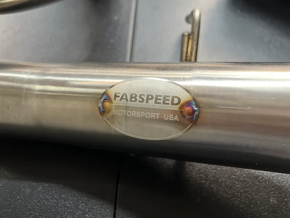 Close-up of a Fabspeed Motorsport USA stainless steel exhaust pipe with a welded badge.