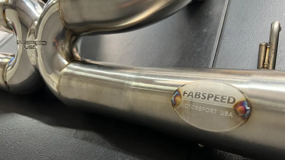A close-up of a Fabspeed Motorsport USA stainless steel exhaust pipe, showcasing the brand logo and welds.