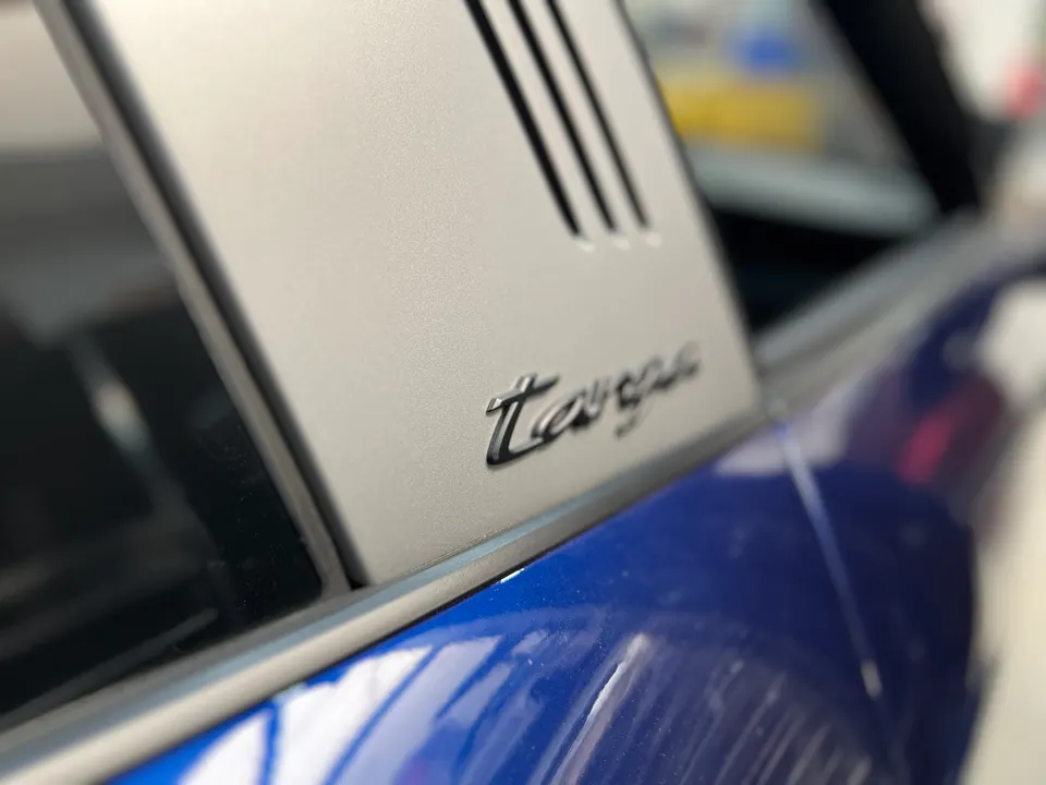 Close-up of a blue Porsche Targa's silver roof pillar with the "Targa" emblem.