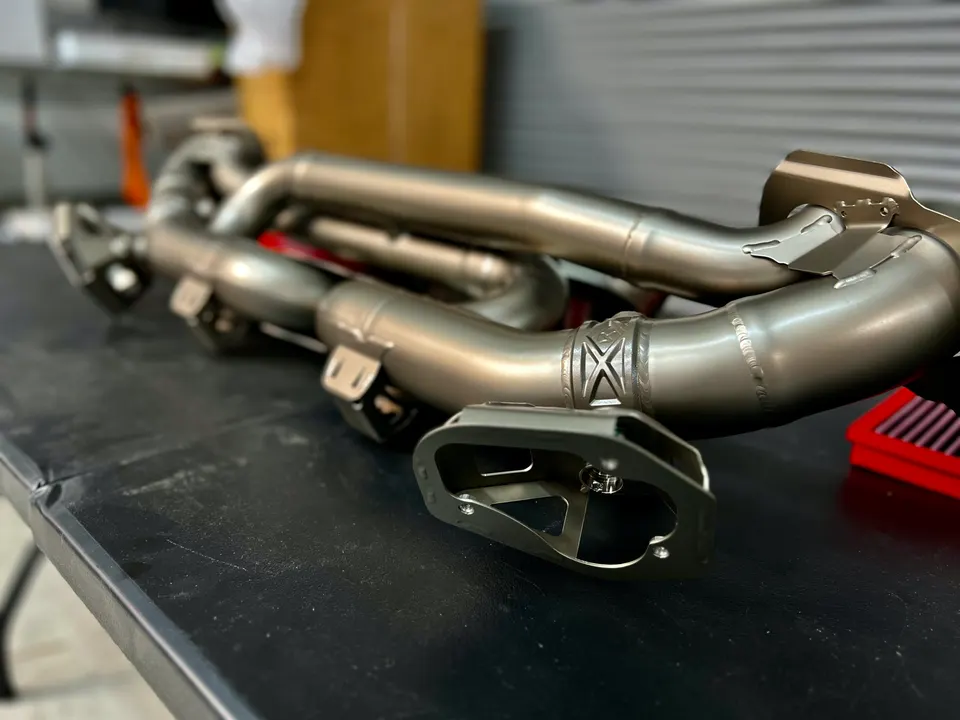 High-performance titanium exhaust headers for a sports car, displayed on a workbench in a tuning shop.