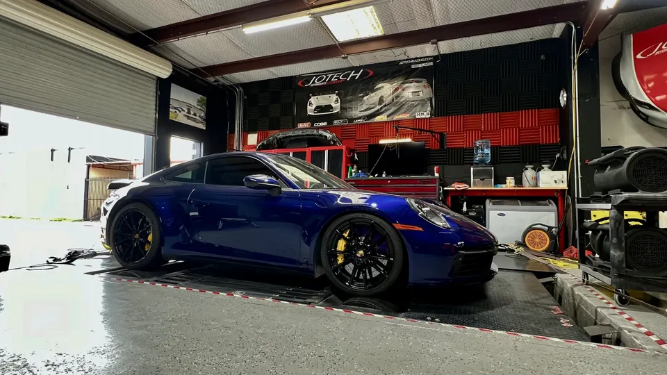 A blue Porsche 911 on a dynamometer at Jotech Motorsports performance tuning shop.