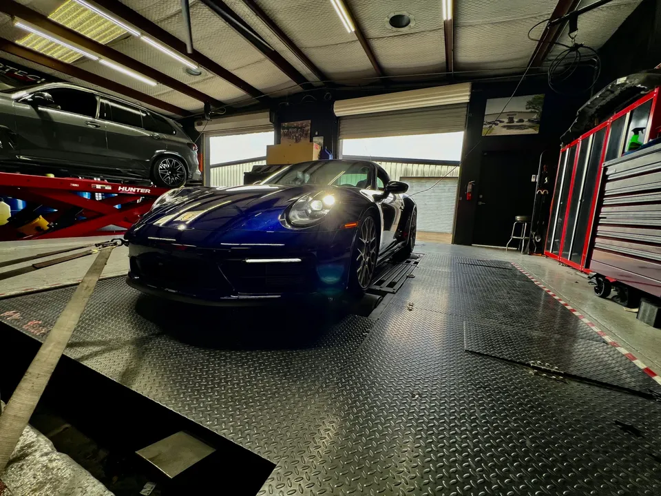 A blue Porsche 911 strapped to a dynamometer in a performance tuning shop, ready for a power run.