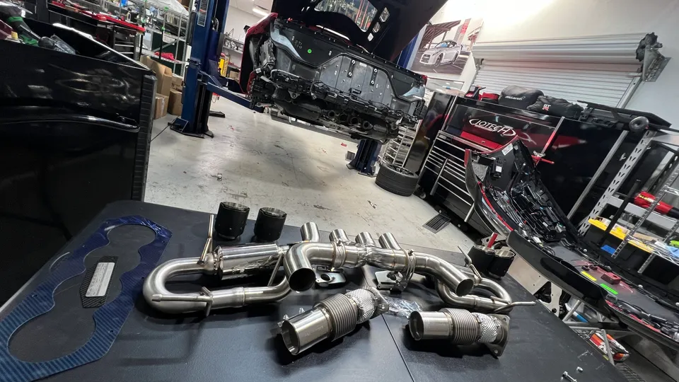 New performance exhaust system laid out on a table in a Jotech Motorsports shop with a car on a lift in the background.