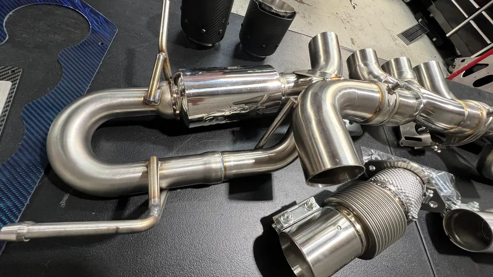 A new stainless steel performance exhaust system with multiple pipes and a muffler laid out in a shop.