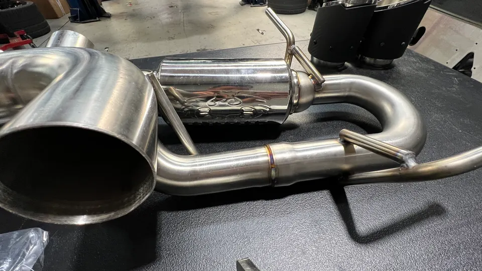 A new stainless steel performance exhaust system with a muffler and piping on a workbench in a shop.