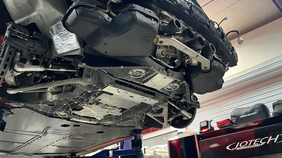 A McLaren car on a lift in a Jotech Motorsports shop, showing the underbody, suspension, and brake components.