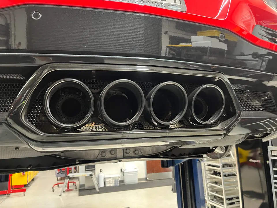 Close-up view of the quad exhaust tips and rear diffuser of a red sports car on a lift in a performance shop.