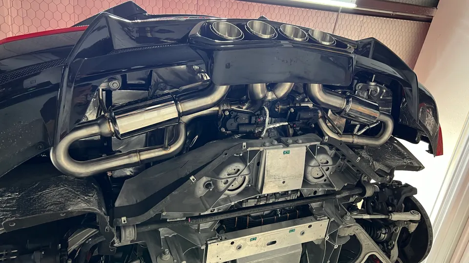 Underside view of a black Corvette C8 on a lift, showcasing a polished aftermarket exhaust system.