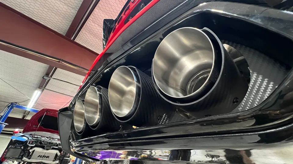 Close-up of a car's quad exhaust tips with carbon fiber trim in a performance tuning shop.
