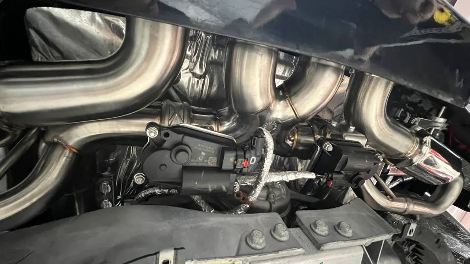 Close-up of stainless steel exhaust headers and downpipes with heat shielding installed on a performance car.