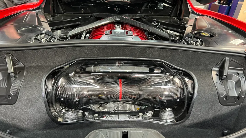 Close-up of a red Corvette C8 mid-engine bay featuring a supercharger and carbon fiber engine cover.