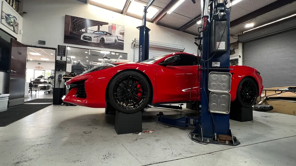 Red C8 Corvette on a car lift in a Jotech Motorsports performance tuning shop.