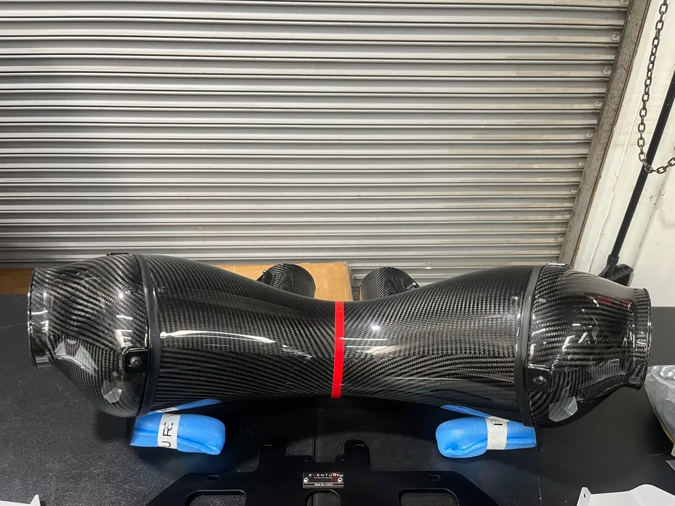 Eventuri carbon fiber intake system on a workbench in a performance tuning shop, ready for installation.