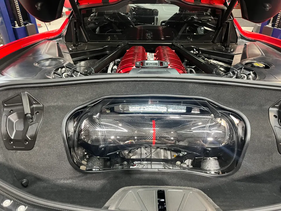 Close-up view of a red Corvette C8 engine bay featuring a red intake manifold and carbon fiber engine cover.