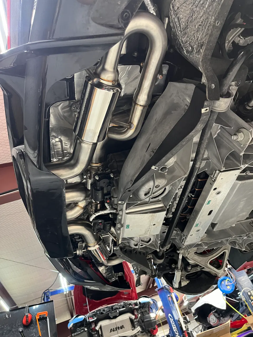 Underside view of a performance car on a lift, showcasing a newly installed stainless steel exhaust system and muffler.