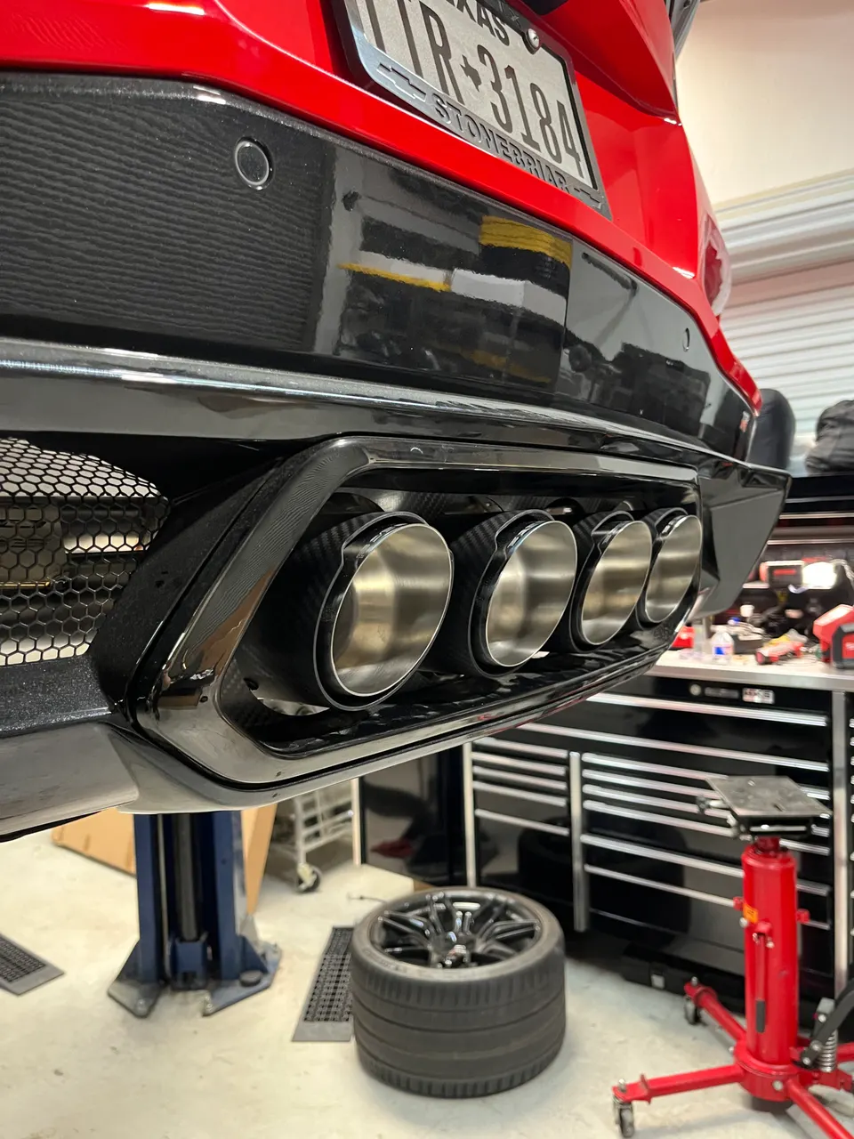 A red C8 Corvette's rear exhaust and diffuser on a lift in a performance shop.