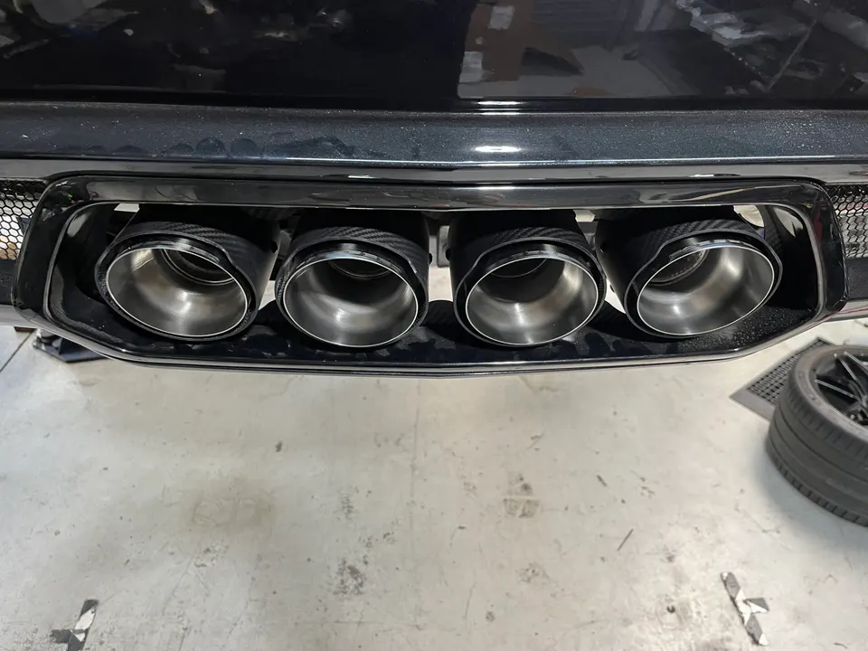 Close-up of a car's quad exhaust tips with carbon fiber surrounds, likely in a performance shop.