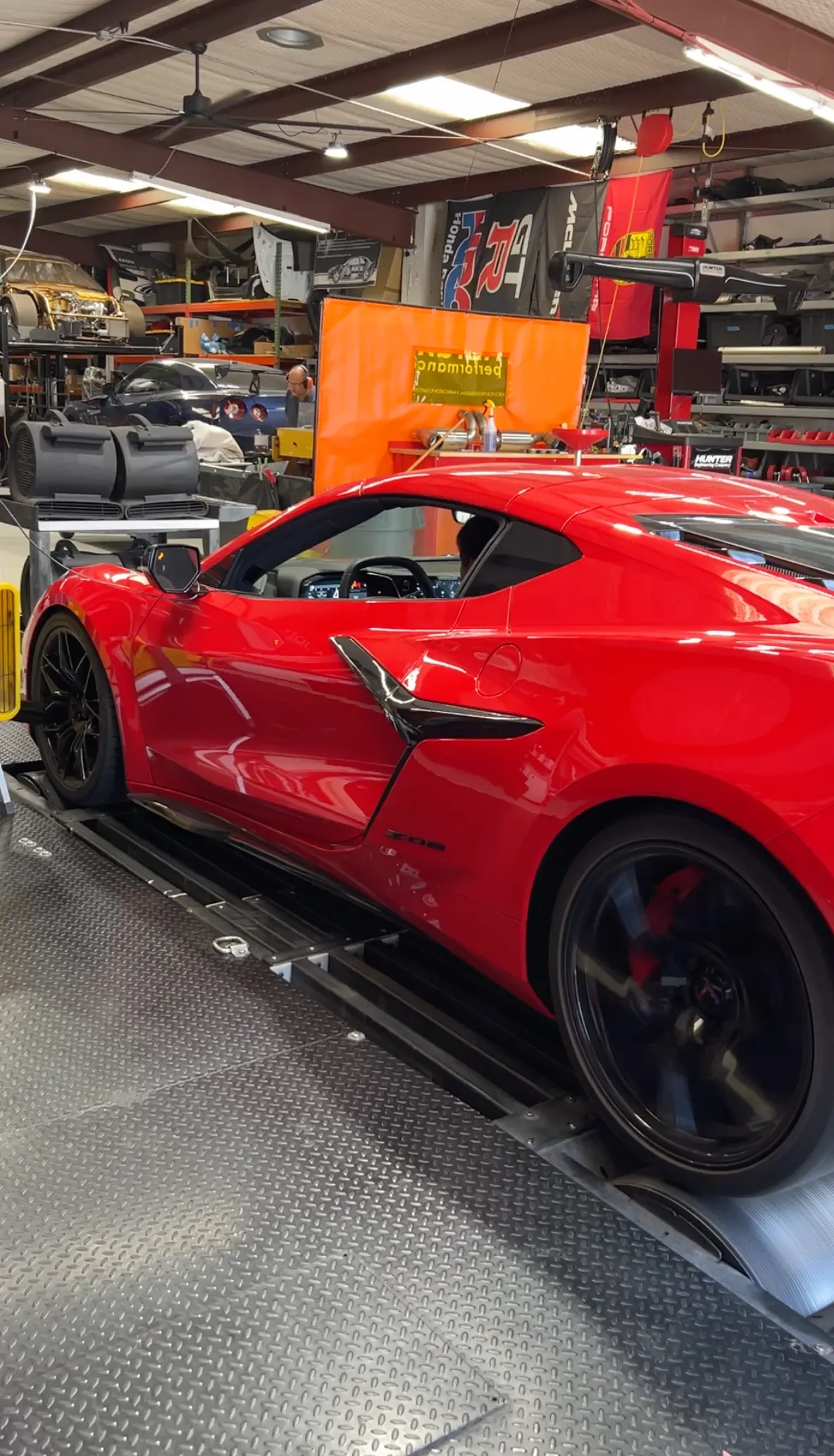 Red Chevrolet Corvette C8 Z06 strapped to a dynamometer in a performance tuning shop, undergoing a power test.