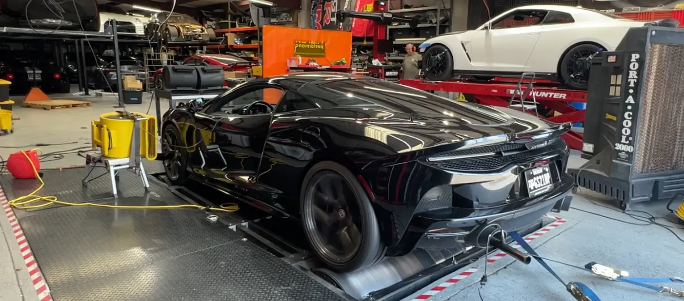 Black McLaren supercar on a dynamometer at a performance tuning shop, undergoing power testing.