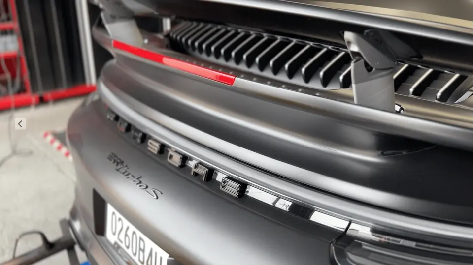 Rear view of a grey Porsche 911 Turbo S on a dyno, showcasing the PORSCHE lettering and turbo S badge.