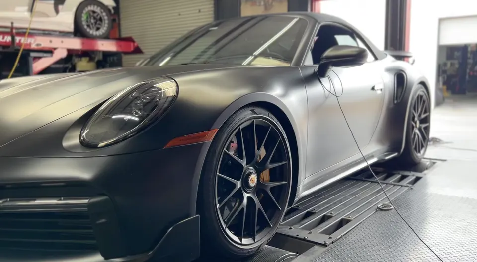 Matte black Porsche 992 911 Turbo S strapped to a dynamometer for performance tuning.