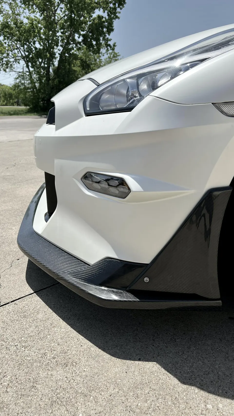 Close-up of a white Nissan GT-R's front bumper featuring a carbon fiber splitter and LED daytime running lights.