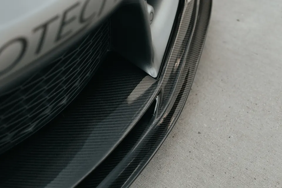 A close-up of a car's front bumper featuring a carbon fiber splitter and grille.