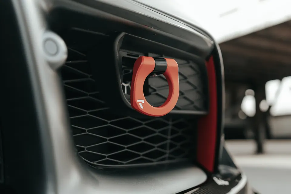 Close-up of a red tow hook mounted on the front bumper grille of a performance car.