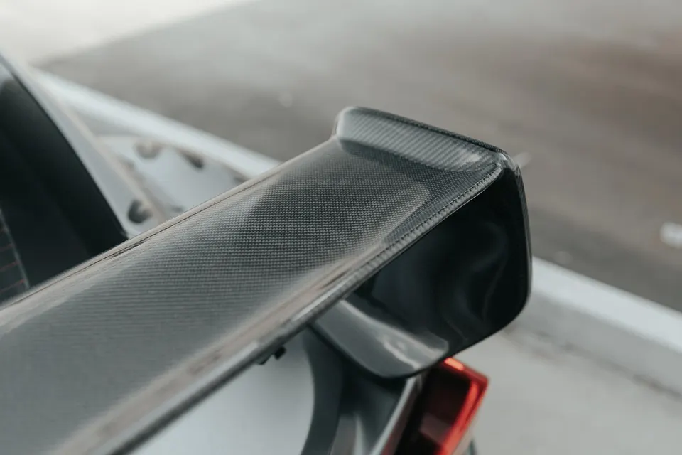 Close-up shot of a carbon fiber rear wing on a performance car, highlighting the weave pattern and sleek design.