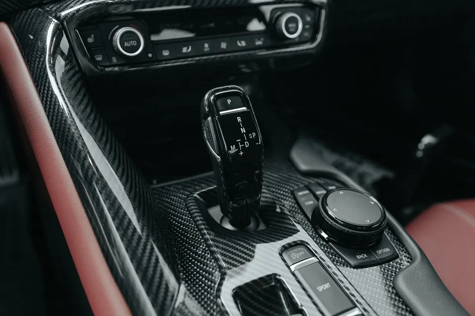 Close-up of a car's interior featuring carbon fiber trim, automatic shifter, and red leather accents on the center console.
