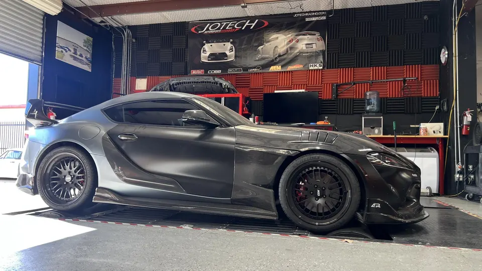 A grey Toyota Supra with carbon fiber body panels on a dyno at Jotech Motorsports for performance tuning.