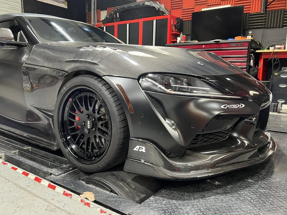 Custom carbon fiber Toyota Supra on a dyno at Jotech Motorsports, showcasing aftermarket wheels and front aero.