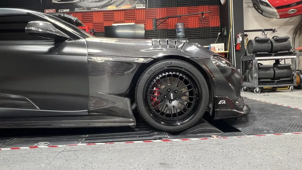 Custom widebody Toyota Supra on a dyno, featuring carbon fiber body panels, black custom wheels, and red brake calipers.