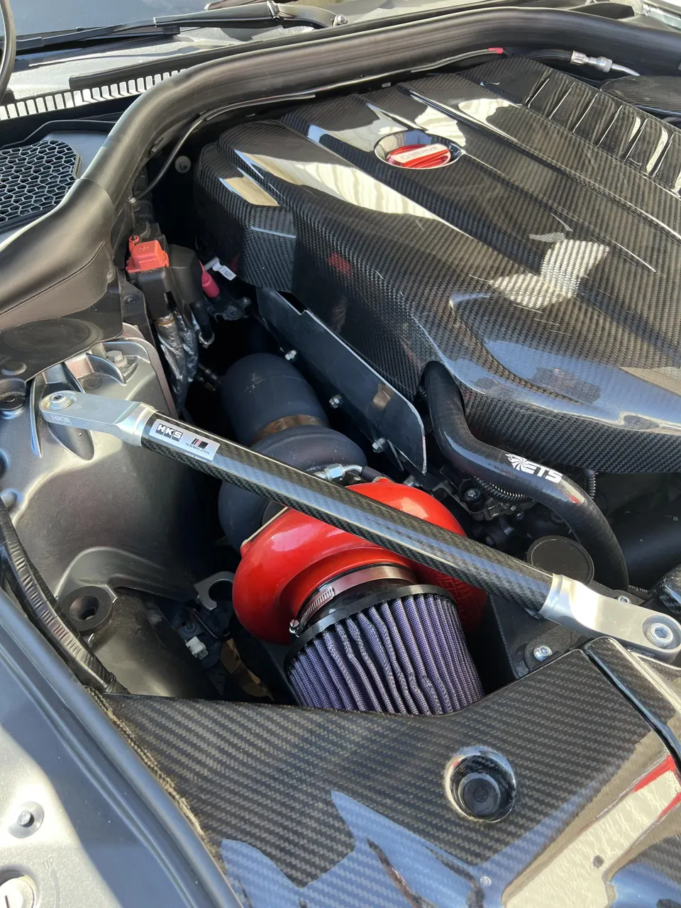 Close-up of a modified Toyota Supra engine bay with a red turbocharger, aftermarket air intake, and carbon fiber engine cover.