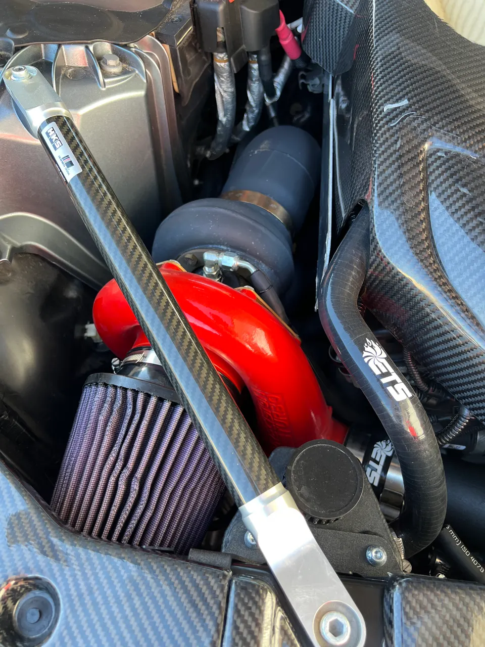Close-up of a high-performance engine bay featuring a red turbocharger, aftermarket air filter, and carbon fiber components.