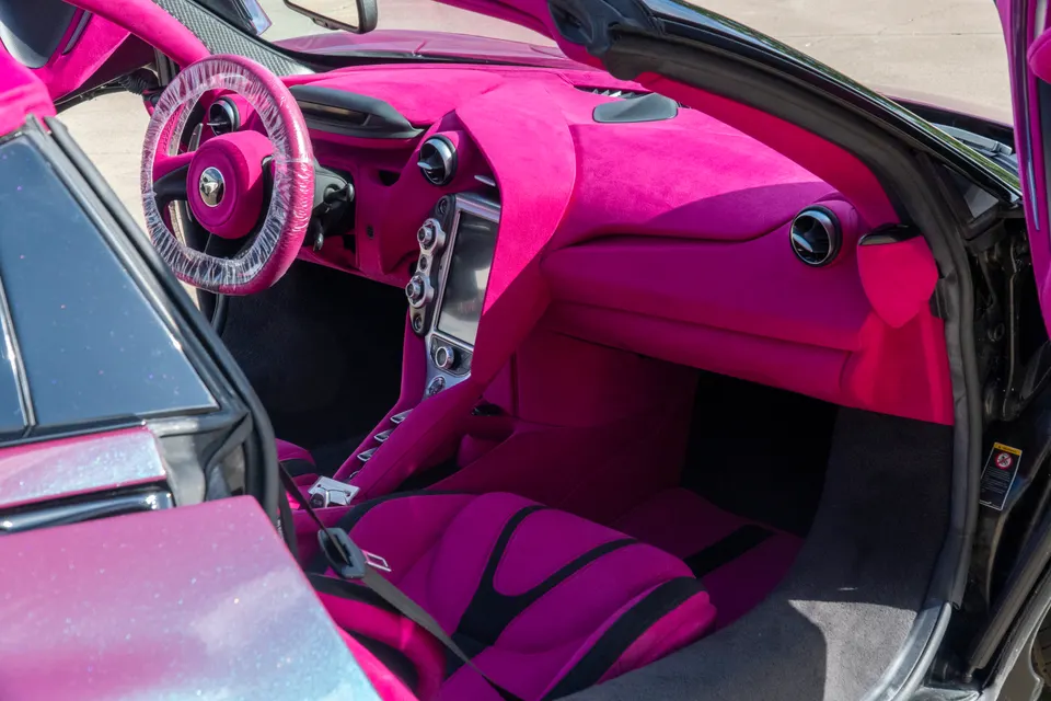 A close-up of a McLaren's custom pink interior, featuring the dashboard, steering wheel, and seats.