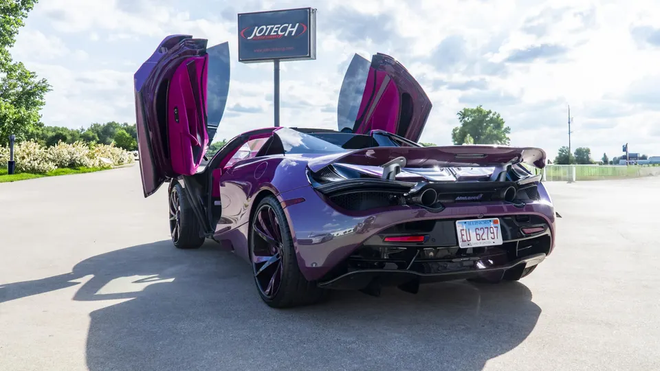A stunning purple McLaren 720S with its butterfly doors open, parked outdoors with a Jotech sign visible in the background.