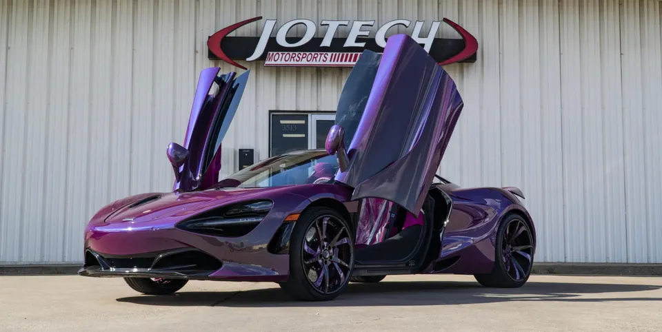 A purple McLaren 720S with its butterfly doors open, parked in front of the Jotech Motorsports building.