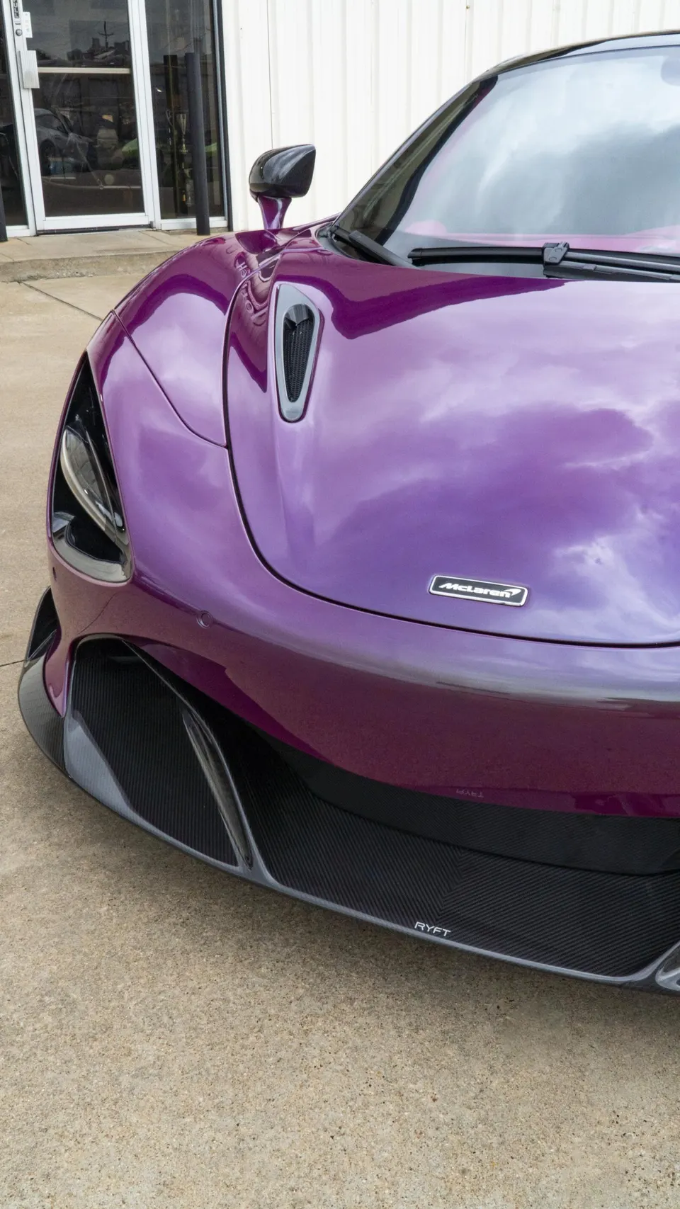 Close-up of a purple McLaren supercar's front end, showcasing its carbon fiber splitter and sleek design.